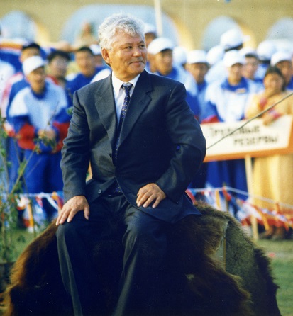 МЕНиколаев сидит на шкуре медведя. за ним Дети Азии
